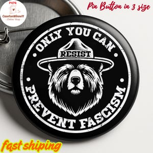 May include: Black pin button with a white illustration of a bear wearing a hat, with the words "ONLY YOU CAN RESIST PREVENT FASCISM" in a circular design. The text "Pin Button in 3 size" is at the top.