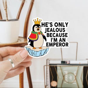 May include: A sticker featuring a cartoon penguin wearing a crown and a red cape, standing on an iceberg. The text reads, "He's only jealous because I'm an emperor."