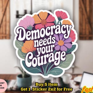 Könnte beinhalten: Ein Aufkleber mit dem Text "Democracy needs your Courage" in Weiß, umgeben von bunten Blumen in Rosa, Orange und Lila. Der Aufkleber ist wasserfest und kann als Magnet verwendet werden.