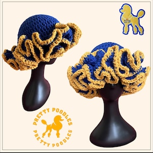 Könnte beinhalten: Zwei blau-goldene Häkelhüte mit Rüschenkrempen werden auf schwarzen Schaufensterpuppenköpfen präsentiert. Die Hüte haben eine runde Krone und eine breite, wellenförmige Krempe. Die Hüte sind in den Farben Blau und Gold gehalten. Das Bild enthält auch ein Logo eines Pudels.