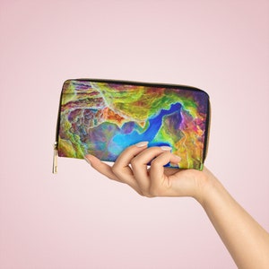 Puede incluir: Una cartera negra con cremallera con un diseño abstracto colorido. La cartera está en una mano con uñas pintadas.