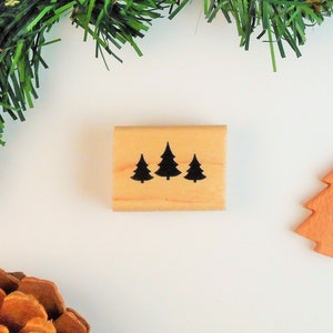 May include: A wooden stamp with three black silhouette Christmas trees on a light brown background.