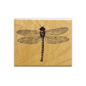 May include: A wooden rubber stamp with a black and white illustration of a dragonfly.