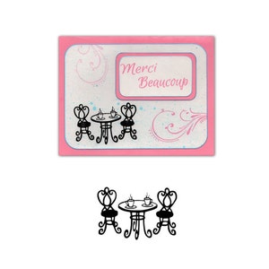 May include: A pink card with a white frame that says "Merci Beaucoup" and a black silhouette of a table and two chairs with cups on the table.