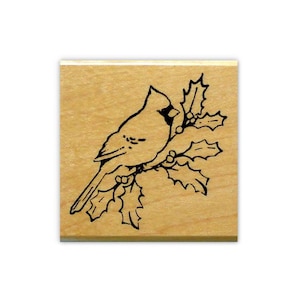 May include: A black and white rubber stamp featuring a cardinal perched on a holly branch. The cardinal is facing left and the holly branch has berries.