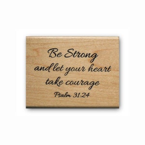 May include: A rectangular wooden plaque with the words "Be Strong and let your heart take courage" and "Psalm 31:24" in black script. The wood has a light brown color.