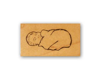 May include: A wooden stamp with a line drawing of a baby sleeping in a blanket.