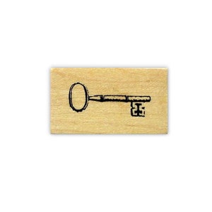 May include: A rectangular wooden stamp featuring a black line drawing of a skeleton key. The key's handle is oval, and the shaft and teeth are detailed. The wood has a light, natural color.