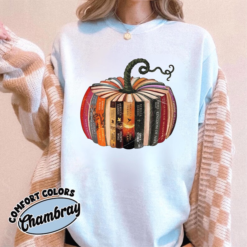 May include: A light blue Comfort Colors Chambray sweatshirt featuring a pumpkin design made of stacked books. The books have colorful spines and a green stem. The text "COMFORT COLORS Chambray" is printed at the bottom.