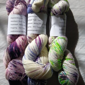 Op de afbeelding: Drie bollen handgeverfde sokkenwol in de kleuren paars, blauw en groen. De wol is superwash merinowol en nylonmix. Elke bol is 400 yards en 100 gram. De wol is fingeringgewicht.