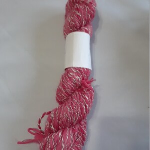 May include: A skein of pink and white yarn with a white label. The yarn is soft and fluffy, and it is perfect for knitting or crocheting.