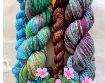 May include: A collection of colorful yarn skeins. The yarn features shades of blue, green, and brown with subtle color variations. The skeins are arranged with decorative pink flowers, suggesting a craft or hobby theme.