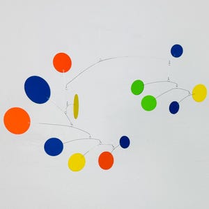 May include: A modern mobile sculpture featuring vibrant orange, blue, green, and yellow discs. The discs are suspended by thin, silver wires against a plain white backdrop, creating a minimalist aesthetic.