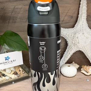May include: A black and silver water bottle with an orange cap. The bottle has a flame design and the text "FreeSip Spout". The cap says "Lift to Unlock". The bottle is 32 oz.