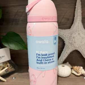 May include: A pink Owala water bottle with a white lid and a built-in straw. The bottle has a light blue label with the text "Hi there. I'm leak proof. I'm insulated. And I have a built-in straw." The bottle holds 32 oz.