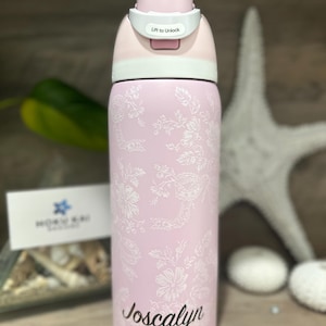 May include: A pink water bottle with a floral design and the name "Joscayln" in cursive. The bottle has a light pink lid with a white lock and the words "Lift to Unlock".