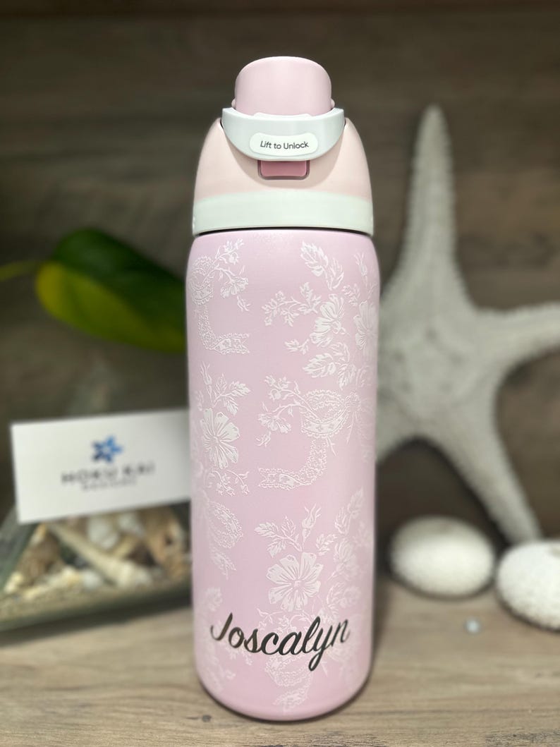 May include: A pink water bottle with a floral design and the name "Joscayln" in cursive. The bottle has a light pink lid with a white lock and the words "Lift to Unlock".