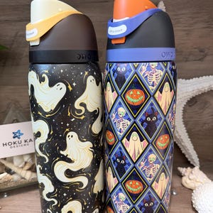 Könnte beinhalten: Zwei Owala-Wasserflaschen mit Halloween-Motiven. Die linke Flasche ist schwarz mit weißen Geistern und Sternen. Die rechte Flasche zeigt ein Rautenmuster mit Kürbissen, Skeletten, Geistern und schwarzen Katzen. Beide haben einen Klappdeckel.