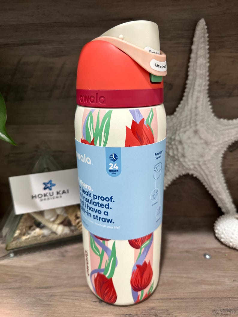 May include: A white insulated water bottle with a red and pink lid, featuring a floral design with red tulips. The bottle has a straw and is labeled "awala". The bottle is leak proof and insulated.