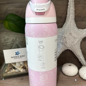 May include: A pink insulated water bottle with a white lid and a floral pattern. The lid has a "Lift to Unlock" mechanism. A label shows the FreeSip spout design. The bottle is next to a starfish and decorative items.