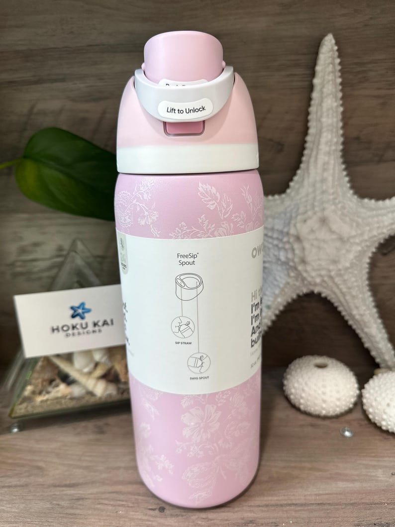 May include: A pink insulated water bottle with a white lid and a floral pattern. The lid has a "Lift to Unlock" mechanism. A label shows the FreeSip spout design. The bottle is next to a starfish and decorative items.