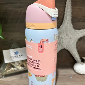 May include: A colorful Owala water bottle with a pink, light blue, and orange design. The bottle features a flip-top lid and a wraparound label with text and food illustrations. The text on the label says "leak proof" and "insulated".