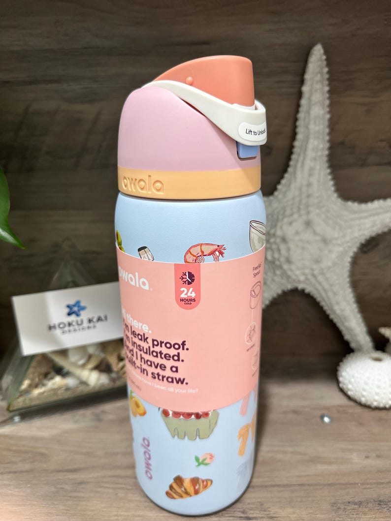 May include: A colorful Owala water bottle with a pink, light blue, and orange design. The bottle features a flip-top lid and a wraparound label with text and food illustrations. The text on the label says "leak proof" and "insulated".