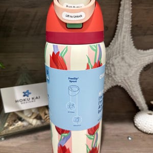 May include: A stainless steel water bottle with a floral design. The bottle has a red and white color scheme with a push-button lid that says "Lift to Unlock". The bottle has a FreeSip spout and is 16 oz.