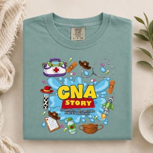 May include: A sage green t-shirt featuring a graphic print with the text "CNA STORY TO INFINITY AND BEYOND FOR OUR PATIENTS". The design includes medical illustrations of a first aid kit, stethoscope, bandages, pills, a clipboard, and a face mask.