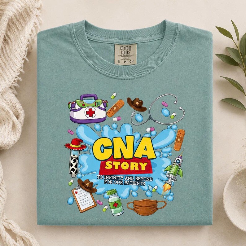 May include: A sage green t-shirt featuring a graphic print with the text "CNA STORY TO INFINITY AND BEYOND FOR OUR PATIENTS". The design includes medical illustrations of a first aid kit, stethoscope, bandages, pills, a clipboard, and a face mask.