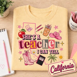 May include: A pale yellow t-shirt featuring a graphic print with the text "SHE'S A TEACHER I CAN TELL" and "California". The design includes illustrations of a red apple, a laptop, pencils, a drink, a pink cowboy hat, boots, and a palm tree.