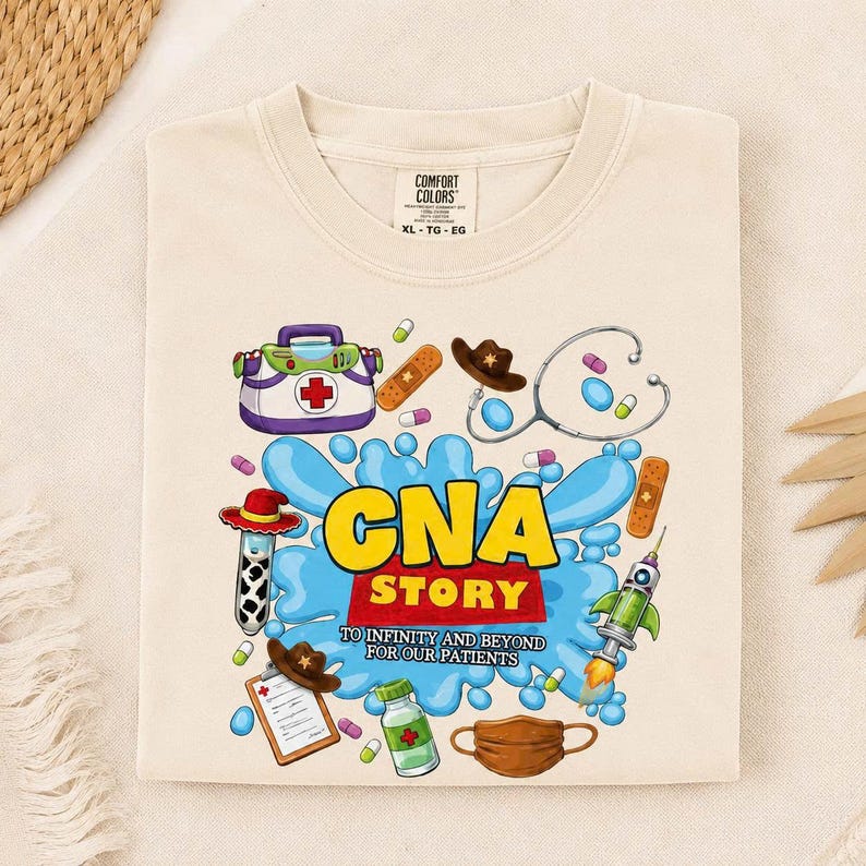 May include: A beige t-shirt featuring a graphic print with the text CNA STORY TO INFINITY AND BEYOND FOR OUR PATIENTS. The design includes a medical bag, stethoscope, cowboy hat, syringe, bandage, clipboard, and face mask on a blue splash background.