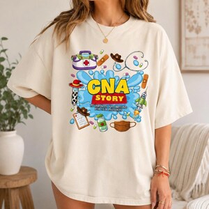 May include: A cream-colored t-shirt featuring a graphic print with the text "CNA STORY TO INFINITY AND BEYOND FOR OUR PATIENTS". The design includes medical icons like a stethoscope, syringe, medical bag, pills, and a face mask.