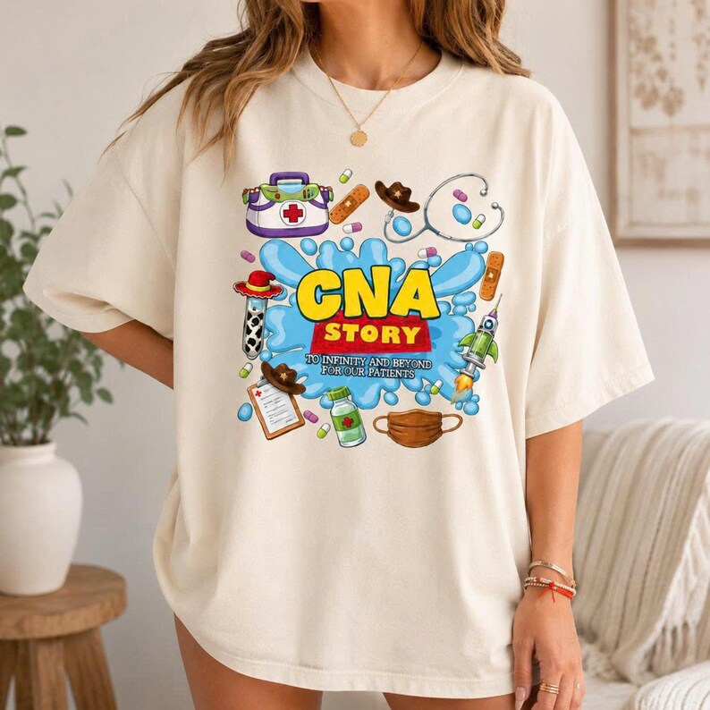 May include: A cream-colored t-shirt featuring a graphic print with the text "CNA STORY TO INFINITY AND BEYOND FOR OUR PATIENTS". The design includes medical icons like a stethoscope, syringe, medical bag, pills, and a face mask.