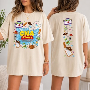 May include: A beige t-shirt featuring a graphic print on the front and back. The front displays the text "CNA STORY TO INFINITY AND BEYOND FOR OUR PATIENTS" surrounded by medical and space-themed illustrations including a stethoscope, pills, and a mask.