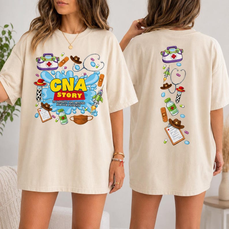 May include: A beige t-shirt featuring a graphic print on the front and back. The front displays the text "CNA STORY TO INFINITY AND BEYOND FOR OUR PATIENTS" surrounded by medical and space-themed illustrations including a stethoscope, pills, and a mask.