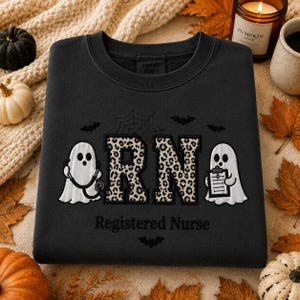 May include: A black crewneck sweatshirt featuring an embroidered design with two white ghosts, one holding a stethoscope and the other a clipboard. The letters RN are filled with a leopard print pattern. The text Registered Nurse is below.