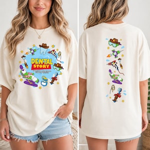 May include: An off-white t-shirt featuring a graphic print with the text DENTAL STORY TO INFINITY AND BEYOND FOR OUR PATIENTS. The design includes a tooth, a dental chair, a toothbrush, and space-themed toys in a colorful cartoon style.