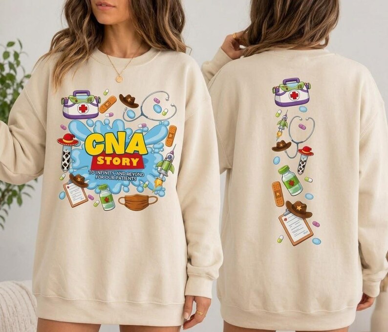 May include: A beige crewneck sweatshirt featuring a graphic print with the text 'CNA STORY TO INFINITY AND BEYOND FOR OUR PATIENTS' surrounded by medical and space-themed illustrations including a first aid kit, stethoscope, and rocket.