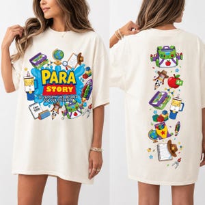 May include: An off-white t-shirt featuring a graphic print of school supplies and toys. The front displays the text "PARA STORY TO INFINITY AND BEYOND FOR OUR STUDENTS" surrounded by a globe, notebook, and backpack. The back shows a vertical arrangement of these items.