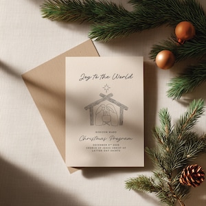 Puede incluir: Una tarjeta de programa navideño color crema con el texto "Joy to the World" y una ilustración del nacimiento. La tarjeta está acompañada de un sobre marrón, ramas de pino y adornos.