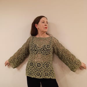 May include: A green crocheted top with a loose fit and long sleeves. The top has a delicate openwork pattern and a round neckline.