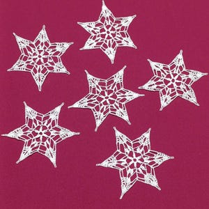 May include: Six white, crocheted star ornaments are arranged on a deep pink background. Each star has a delicate, openwork design with pointed tips. The stars are evenly spaced, creating a visually appealing pattern.