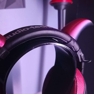 May include: A pair of black headphones with a red headband and red horns. The headphones have the text "audio-tech" printed on the headband.