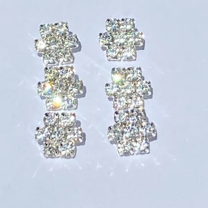 May include: A pair of silver earrings with three crystal-encrusted squares on each earring.