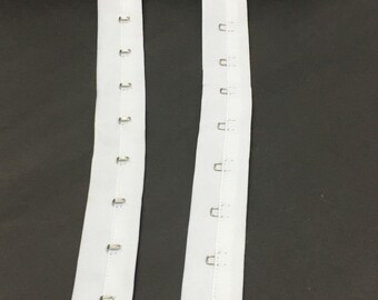 May include: Two white fabric strips with rows of silver metal hooks. The strips are sewn together at the top.