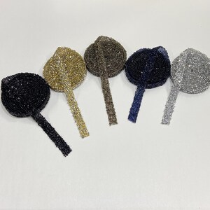 May include: Five spools of rhinestone trim in different colors: gold, brown, navy blue, silver, and black.