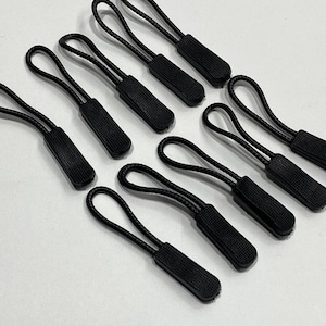 Puede incluir: Diez tiradores de cremallera negros con una superficie texturizada. Los tiradores tienen un bucle en cada extremo y están diseñados para ser unidos a las cremalleras.