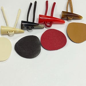Peut inclure: Assortiment de cinq boutons en corne avec des boucles en cuir, et cinq patchs en cuir de différentes couleurs, dont le rouge, le marron, le noir et le blanc.