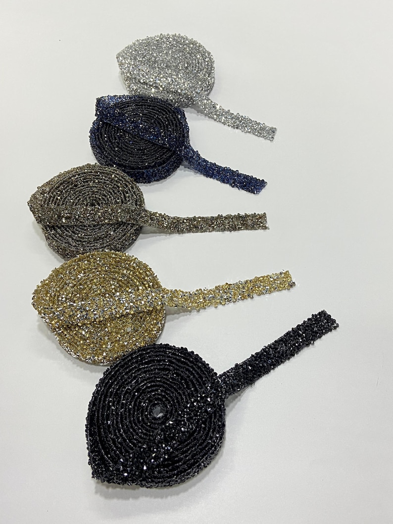 May include: Five spools of beaded trim in different colors. The trim is made of small, sparkly beads and is available in silver, navy blue, brown, gold, and black.